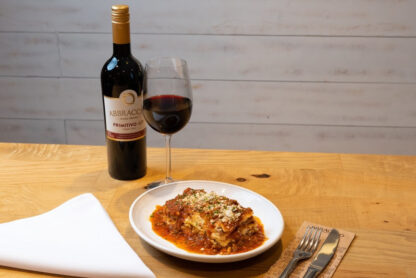 Um prato de lasanha e uma garrafa de vinho sobre uma mesa no Abbraccio.