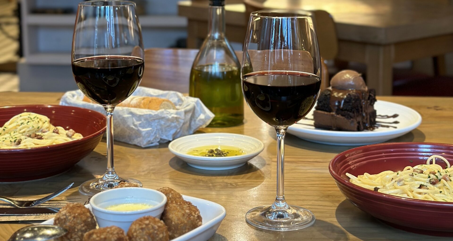 No Abbraccio você pode saborear um delicioso Menu para 2 com duas taças de vinho e uma tigela de macarrão, tudo servido em uma charmosa mesa de madeira.