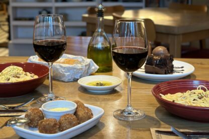 No Abbraccio você pode saborear um delicioso Menu para 2 com duas taças de vinho e uma tigela de macarrão, tudo servido em uma charmosa mesa de madeira.