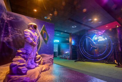 Exposição na Galaxion Exposição, apresentando figura de astronauta em paisagem lunar com portal colorido ao fundo, no Brasil.