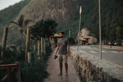 Homem segurando uma câmera em uma calçada perto de uma estrada de montanha.. Imagem ilustra artigo do Barrazine (Barra da Tijuca: um dos melhores locais para ecoturismo no Brasil).