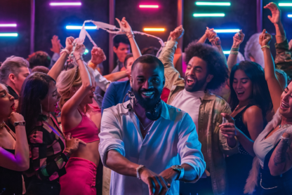 Um DJ negro toca música em uma boate vibrante com uma multidão de pessoas diversas dançando e curtindo a festa sob luzes coloridas de neon durante uma noite no fim de semana.